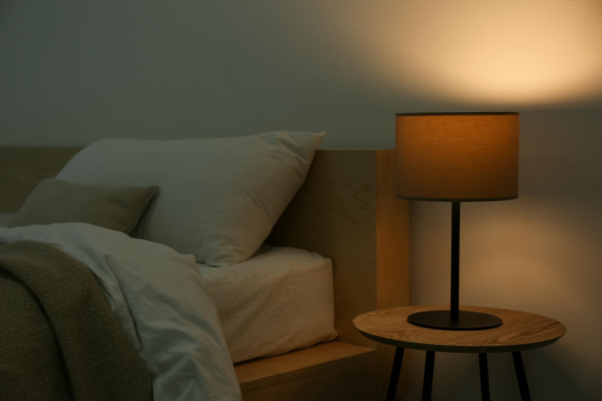 A cozy, peaceful bedroom at night with a soft warm lamp on the bedside table