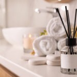 Aromatic reed air freshener and spa stones on white table, space