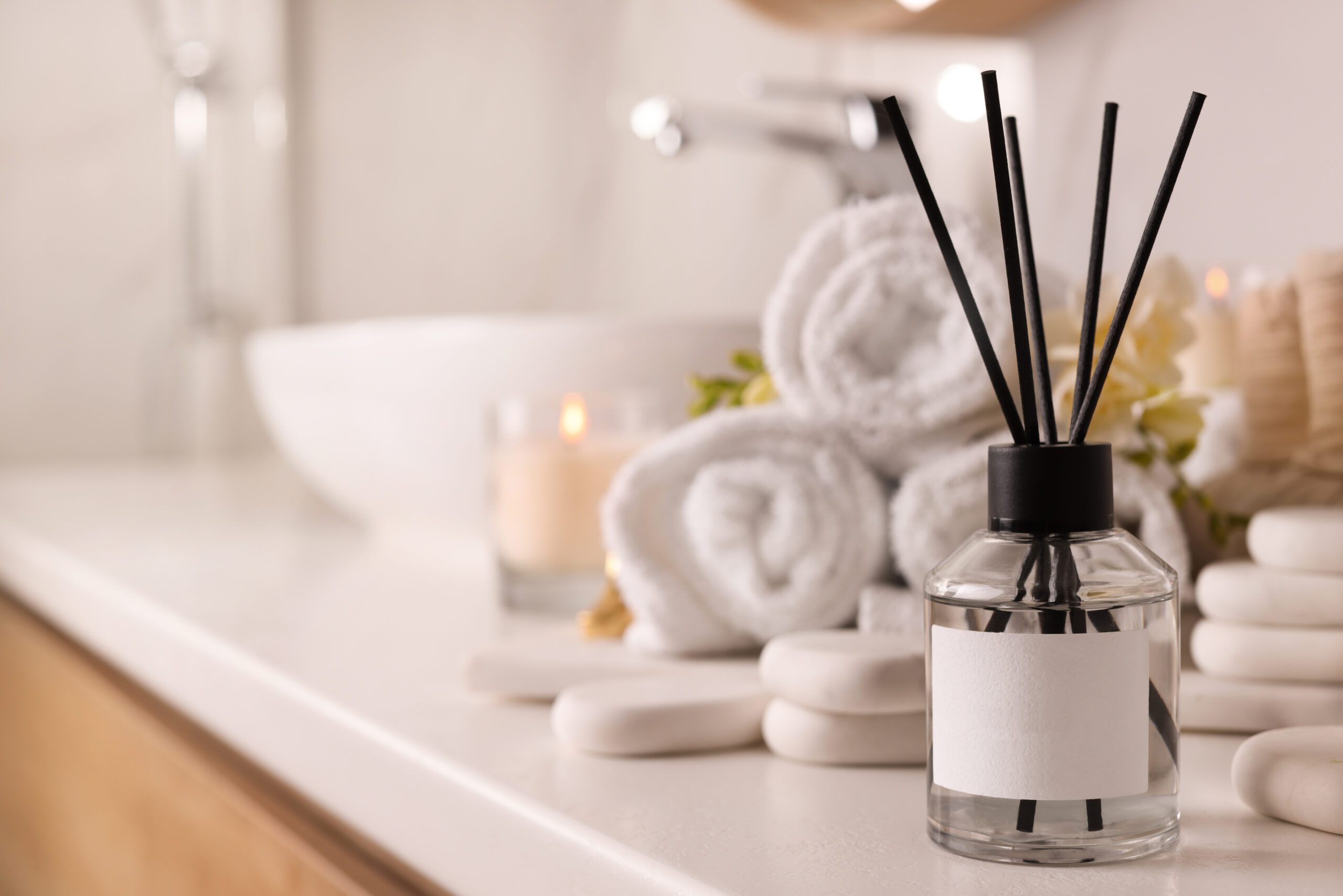 A softly lit bathroom shelf with natural wellness items including eucalyptus, a diffuser, and a warm towel