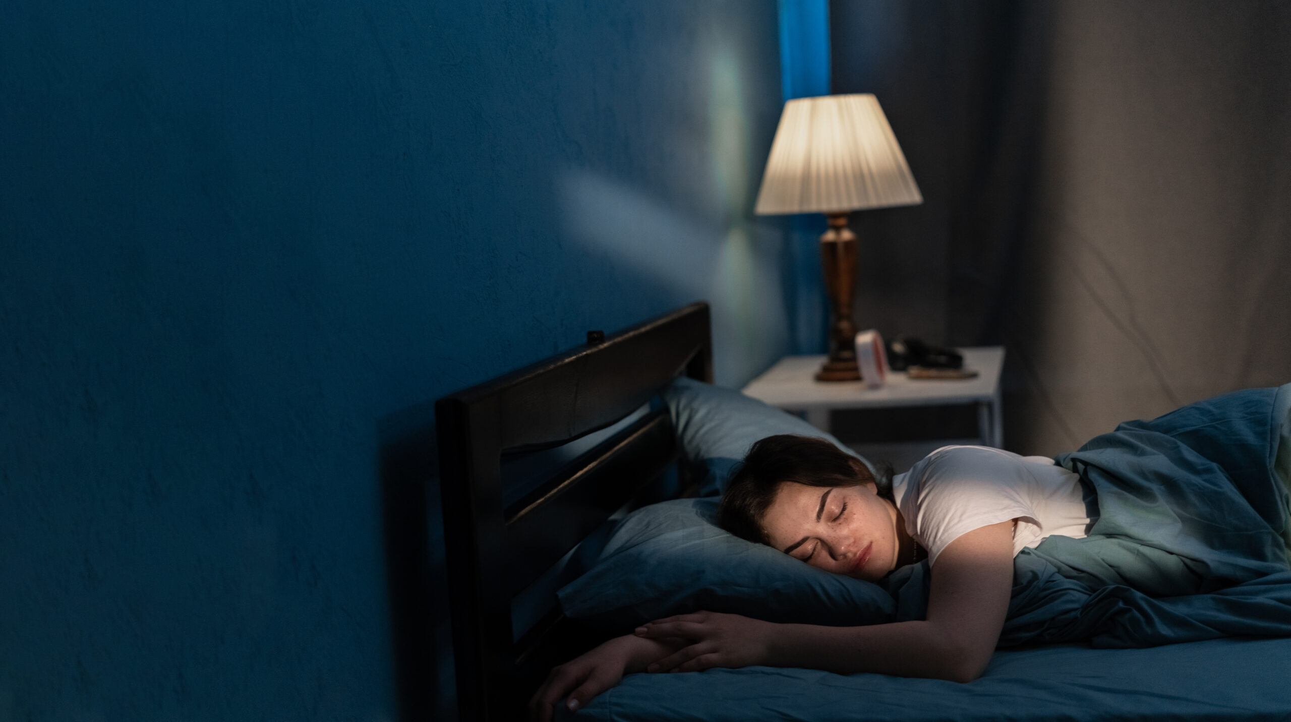 A peaceful bedroom at night with someone sleeping soundly, soft shadows and a gentle lamp glow