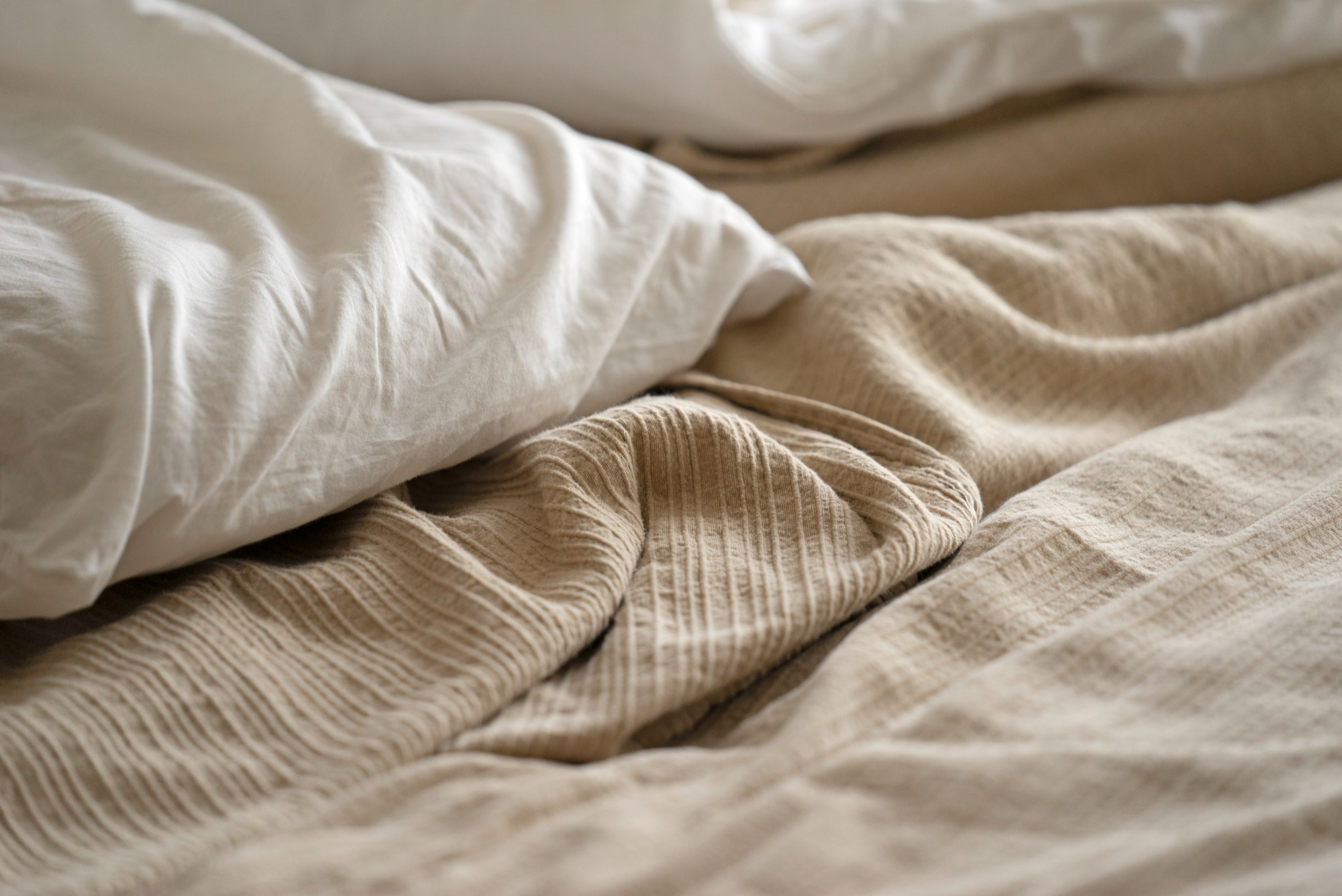 A soft glowing bedside lamp on a nightstand beside a bed with white pillows in a dark cozy bedroom