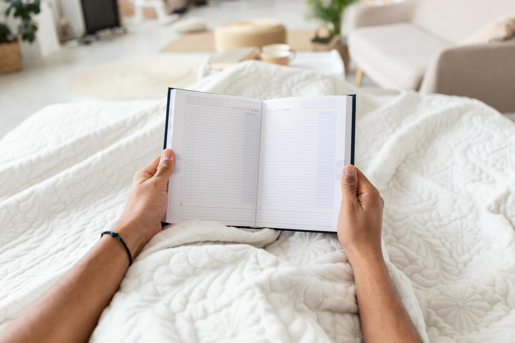 A cozy bed scene with a warm knit blanket, open book, and a glowing candle holder with soft bokeh fairy lights behind