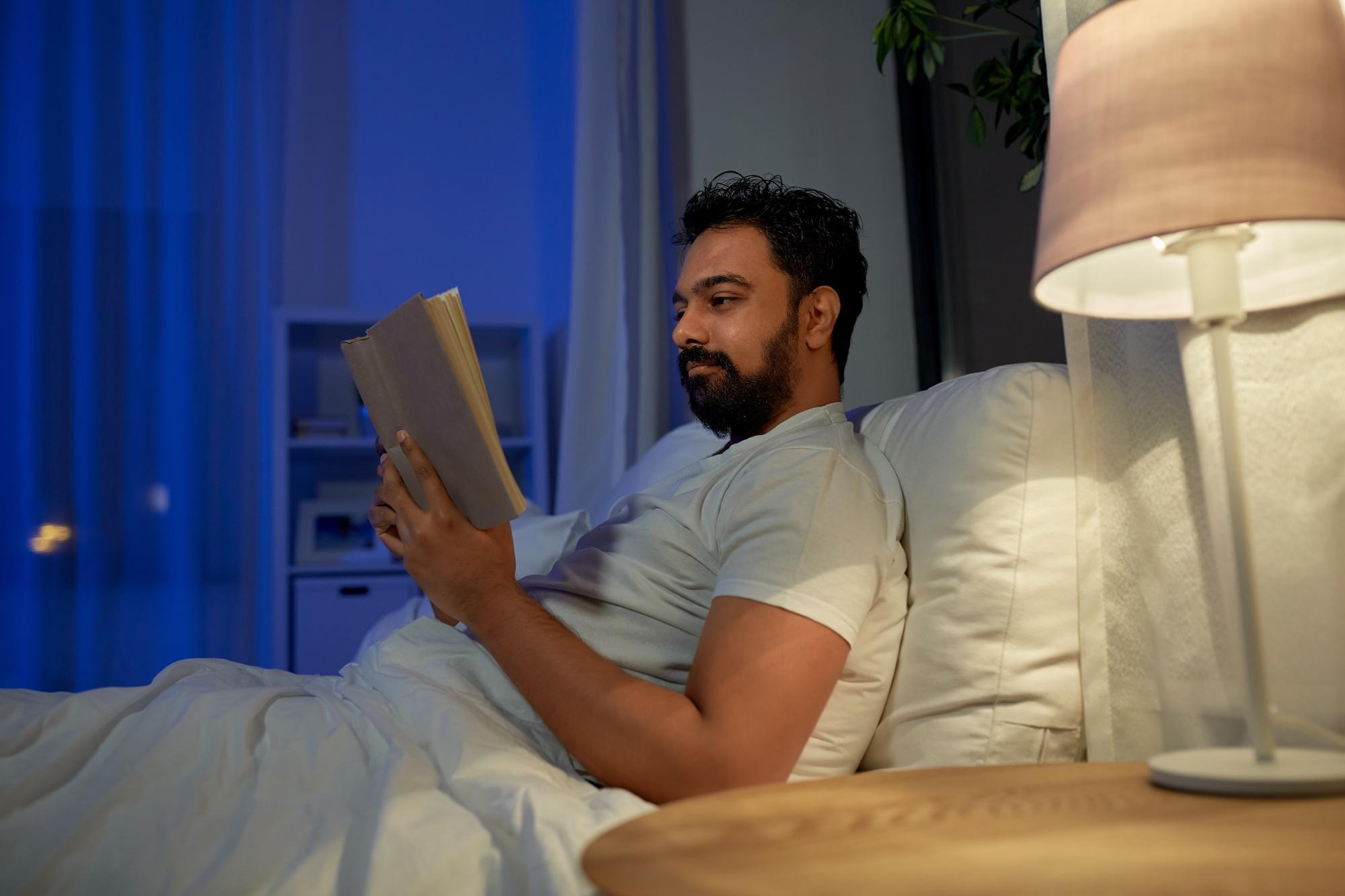 Person reading in bed at night warm lamp.