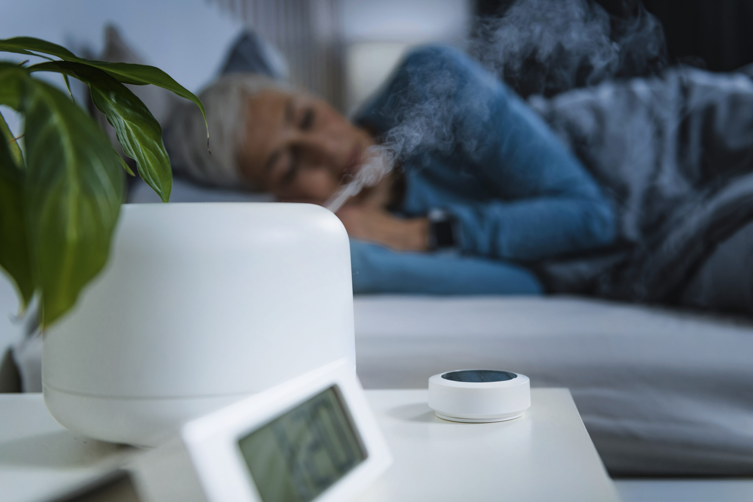 A cozy bedroom at night with a small humidifier on the bedside table and soft warm lamp light