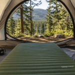 A camping mattress laid out inside a tent with the door open to a forest view