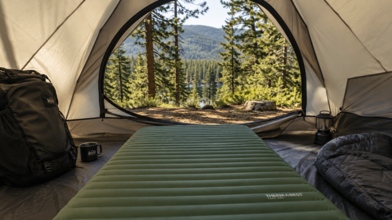 A camping mattress laid out inside a tent with the door open to a forest view