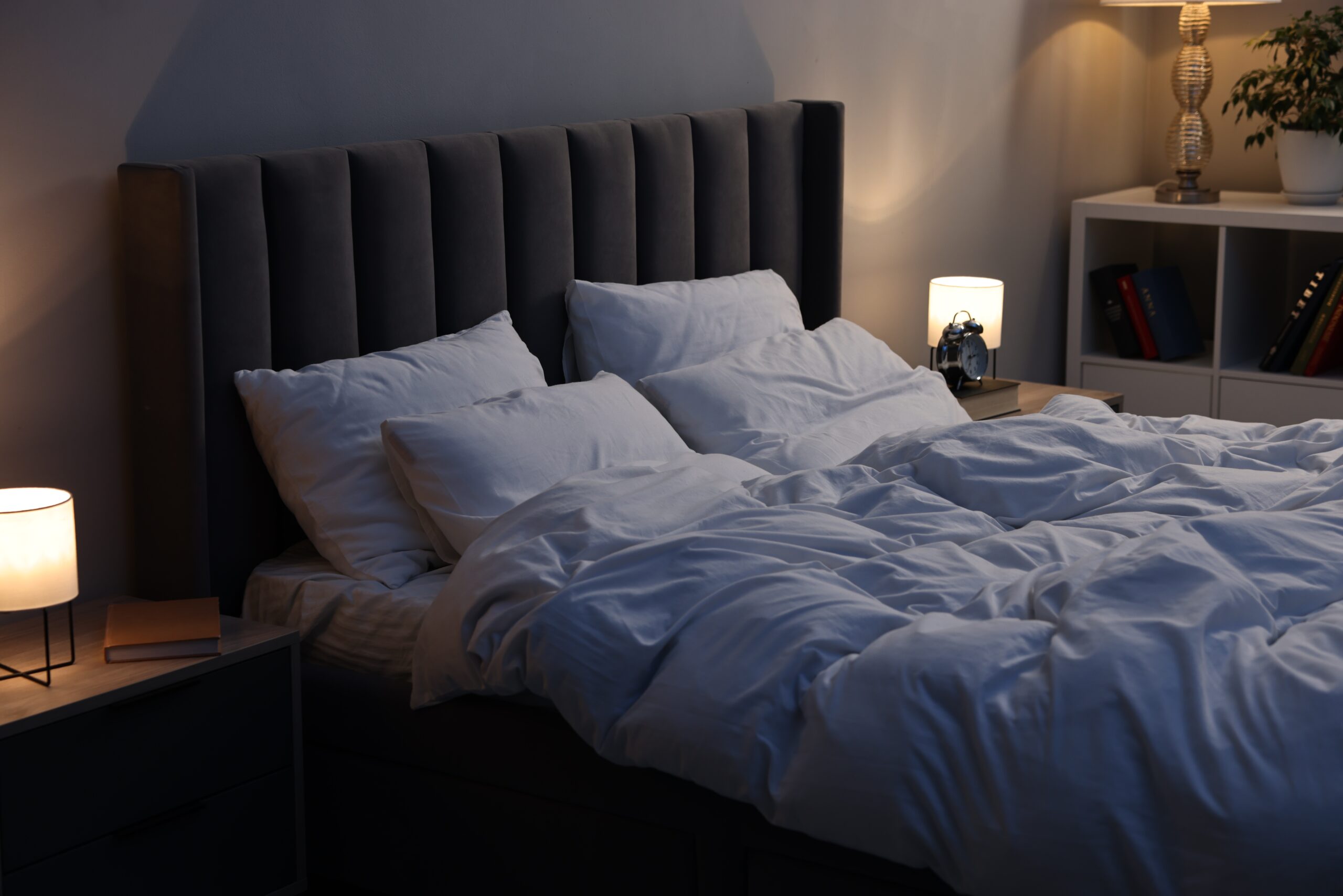 Cozy bedroom at night with soft warm lighting and neatly arranged pillows on a bed