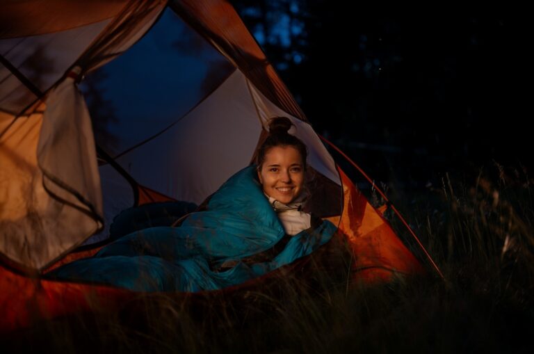 Cozy tent glowing warm at dusk with woman in a sleeping bag