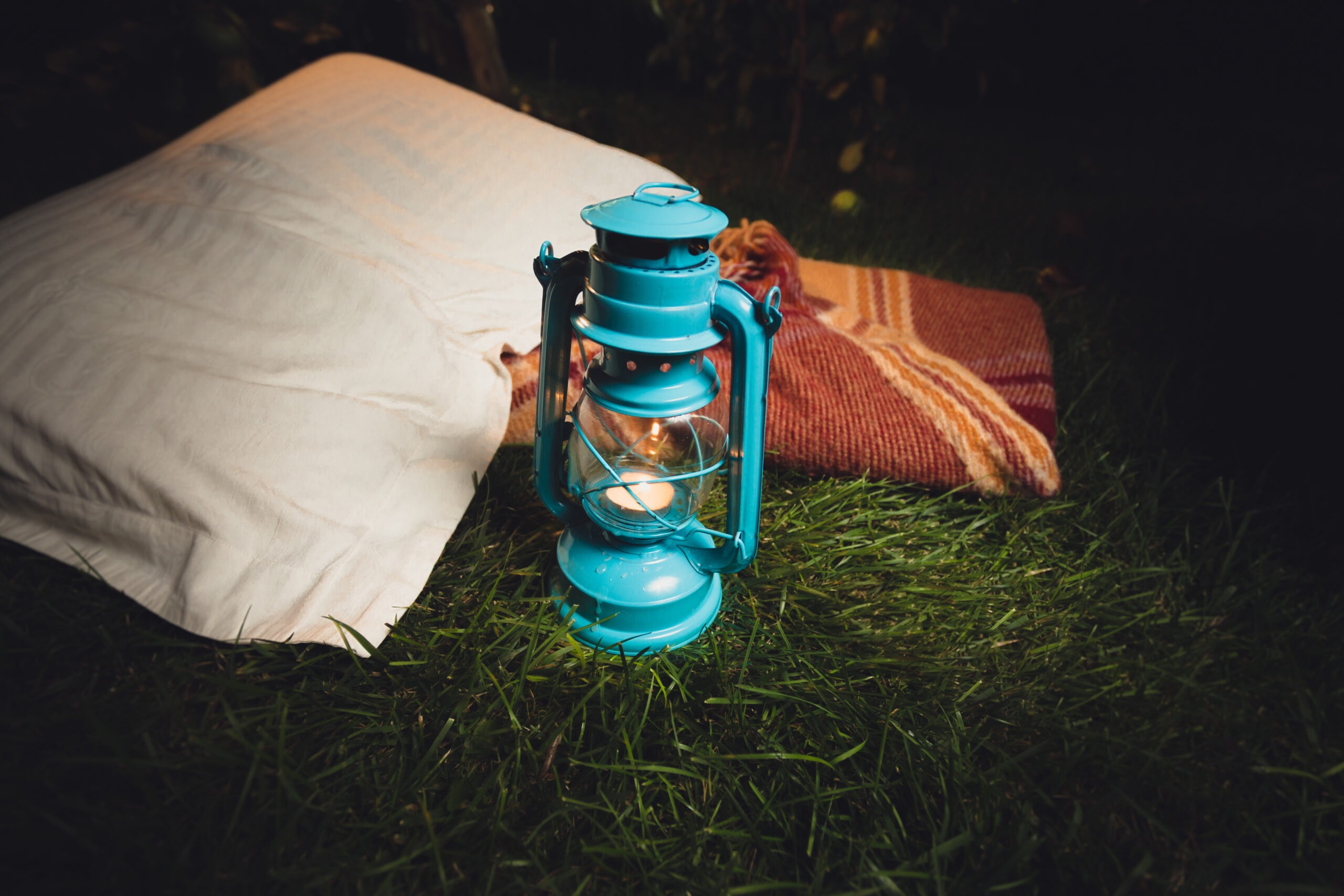 Soft lantern glow inside a tent beside a pillow and folded blanket