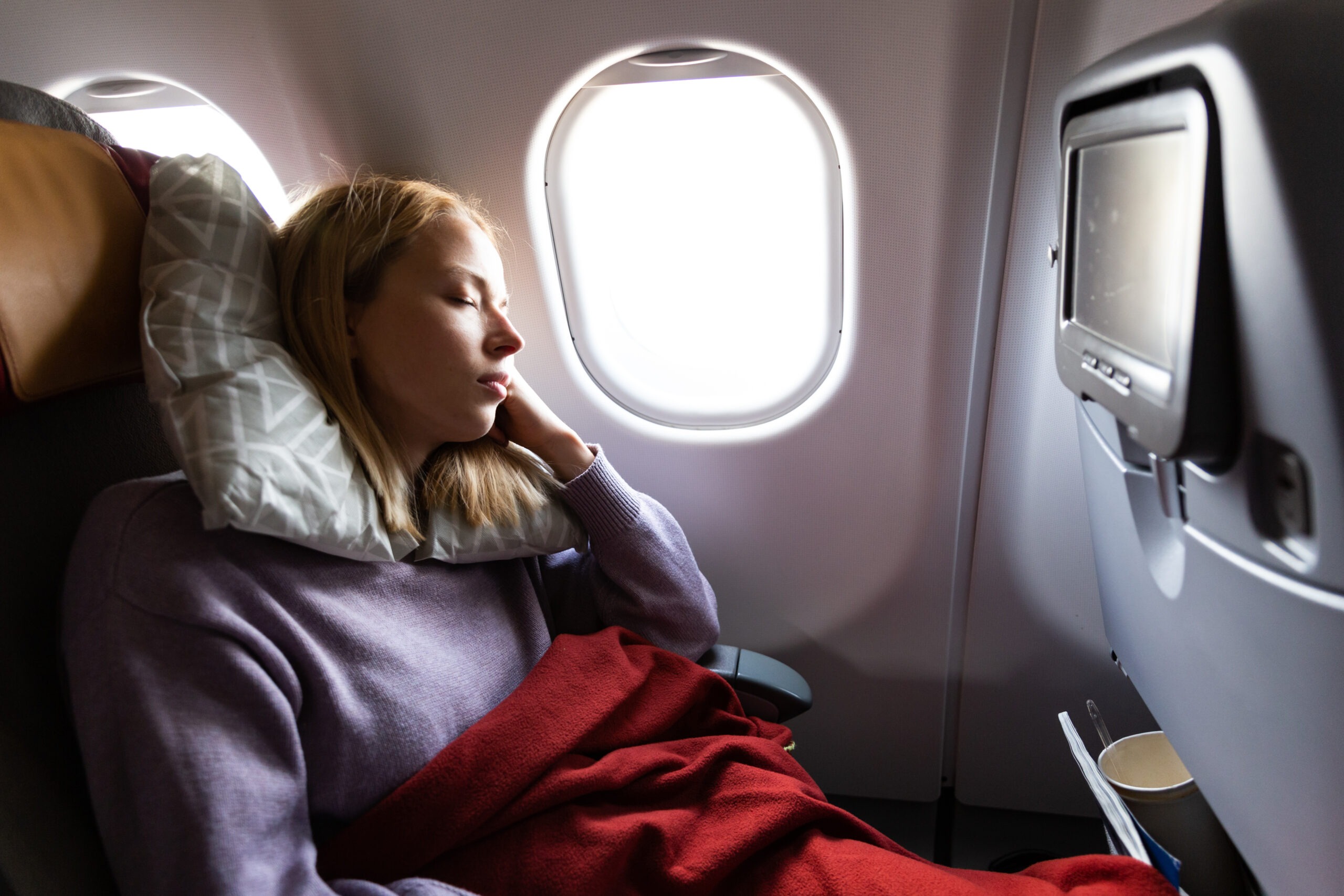 Close-up of a traveler's neck pillow and posture in an economy seat