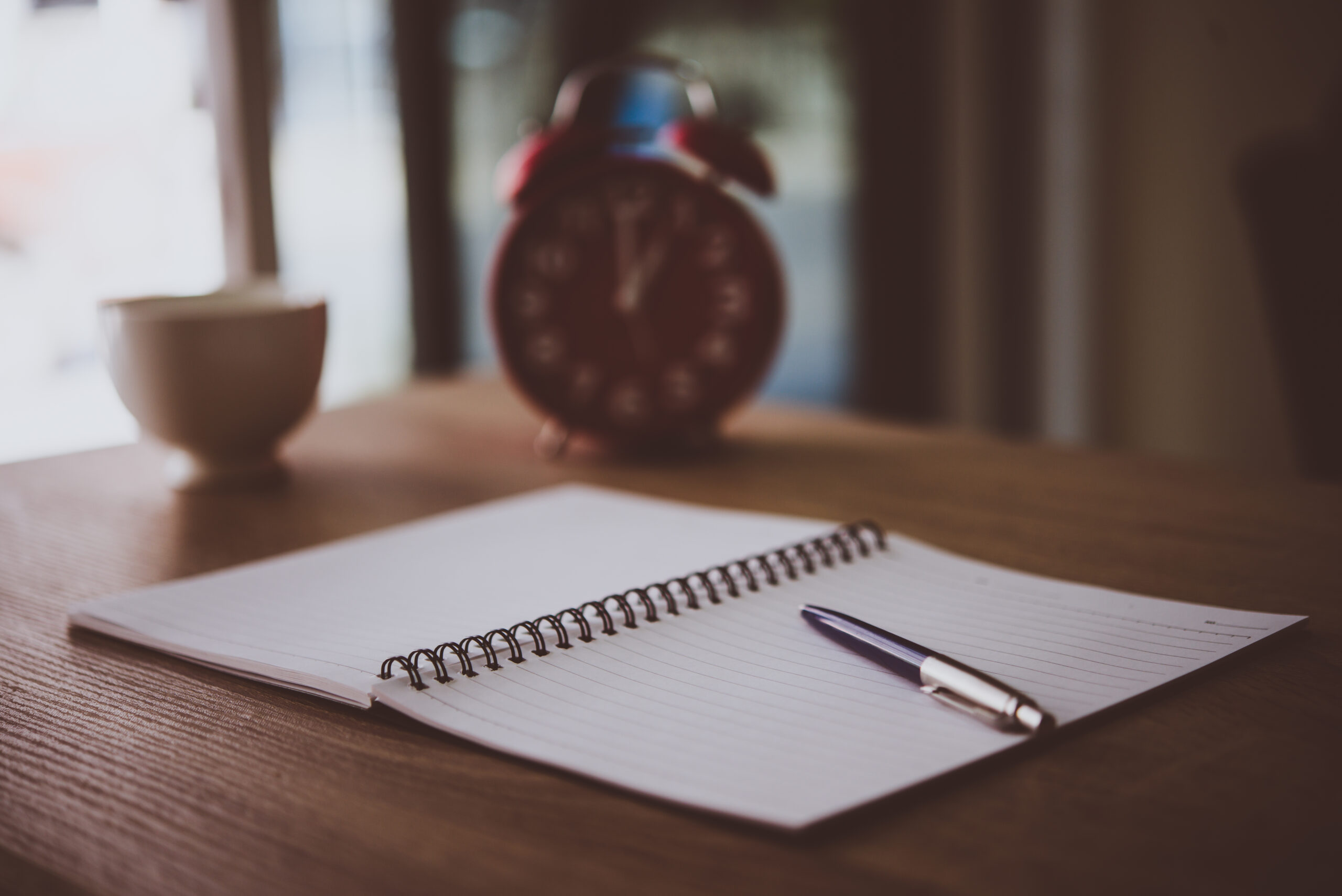 A daily planner open on a wooden desk with morning light and a pen beside it