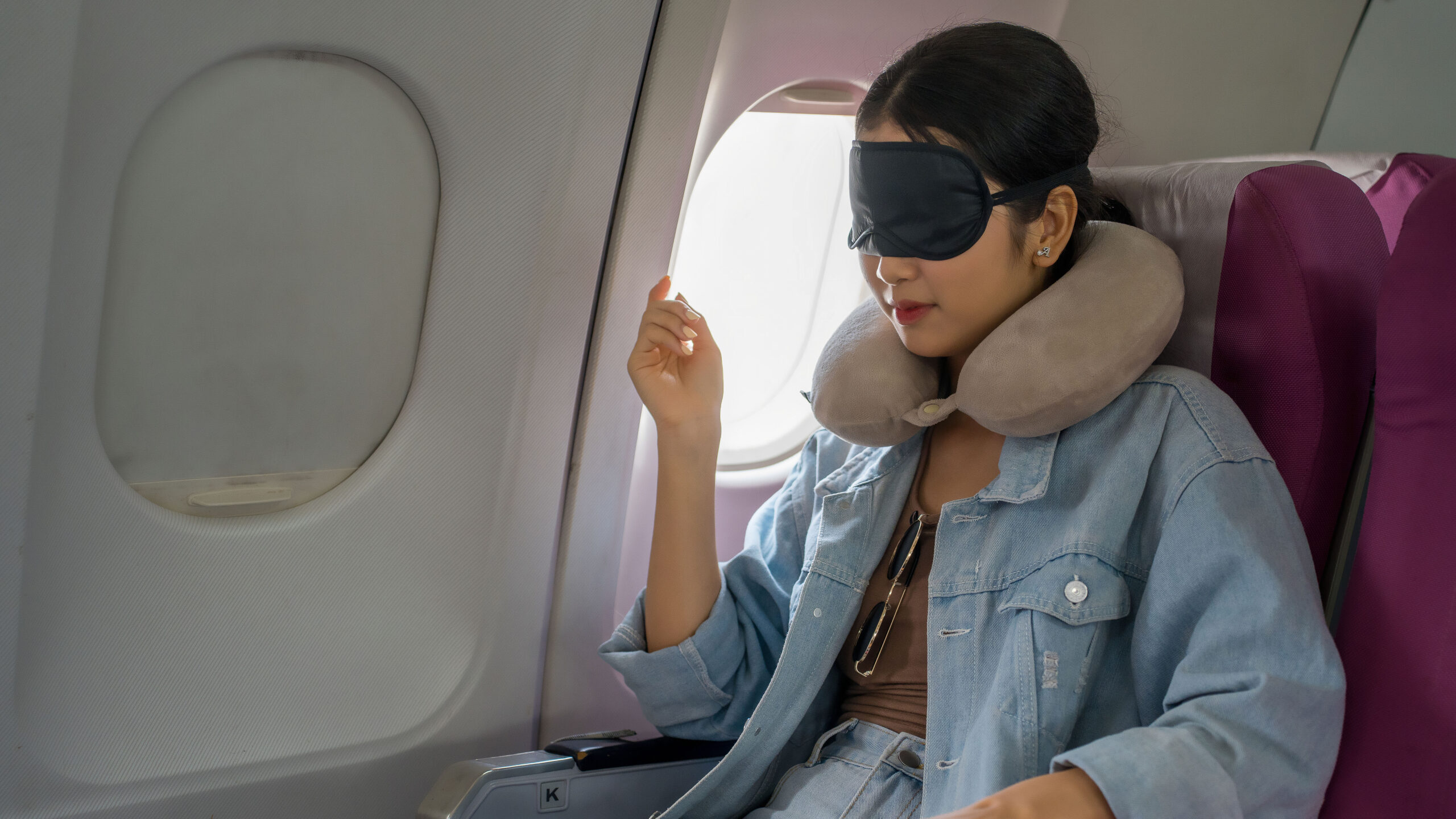 passenger by the airplane window with a neck pillow and eye mask