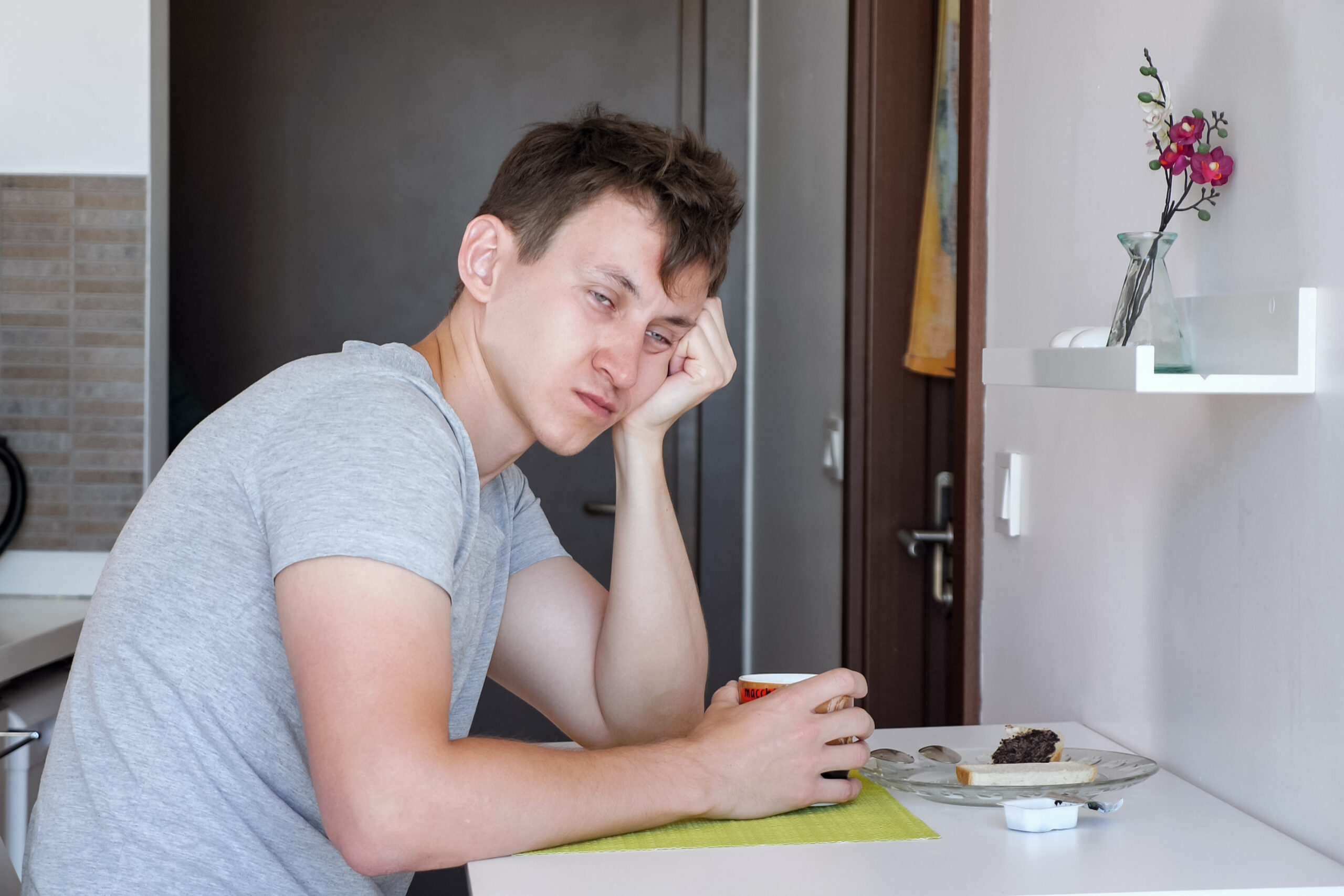 A tired person sitting quietly at a kitchen table in the morning, warm muted tones